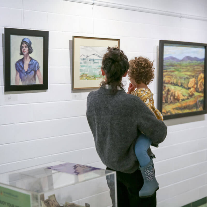 A mother holder her child while viewing art on a wall