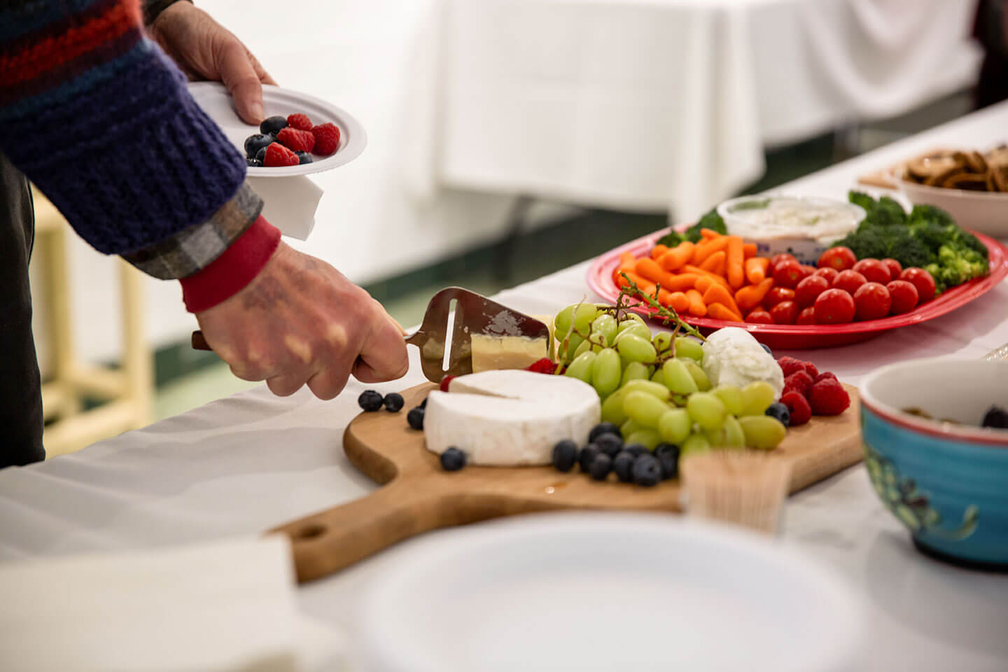 A person cutting cheese on a platter of fruits