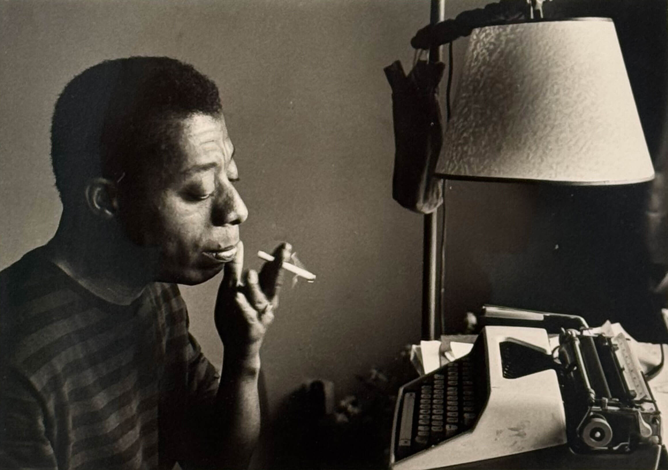 James Baldwin smoking a cigarette looking at his typewriter